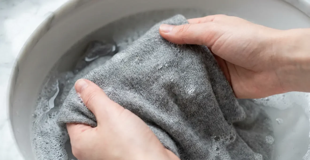 Gros plan sur des mains lavant délicatement un pull en cachemire dans une bassine